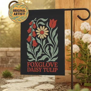 May include: A rectangular black garden flag featuring a botanical illustration of red foxgloves, a yellow daisy, and a red tulip with sage green leaves. The text "FOXGLOVE DAISY TULIP" is printed in red at the bottom. A circular badge reads "ORIGINAL ARTIST!"