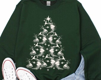 May include: A dark green sweatshirt with a white Christmas tree design featuring a series of cat faces. The tree is topped with a star.