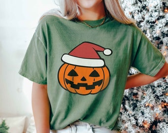 May include: A green t-shirt with a cartoon pumpkin wearing a Santa hat. The pumpkin is orange with a black jack-o'-lantern face.
