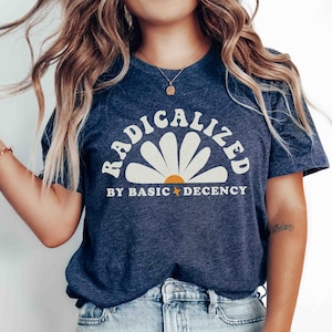 Peut inclure: T-shirt bleu marine avec l'inscription "RADICALIZED BY BASIC DECENCY" dans un motif de marguerite blanche. Le t-shirt a un col rond et des manches courtes. Il est associé à un jean en denim bleu clair.