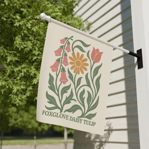 May include: A cream-colored garden flag featuring a floral design with foxgloves, a daisy, and a tulip. The flowers are in shades of peach, orange, and green. The text "FOXGLOVE DAISY TULIP" is printed at the bottom of the flag.