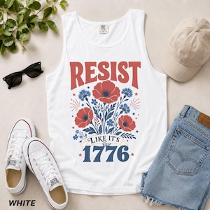 May include: A white tank top featuring a graphic print with the red text RESIST, blue text LIKE IT'S 1776, and a central illustration of red poppies and blue cornflowers. The design includes small star accents and decorative line work.