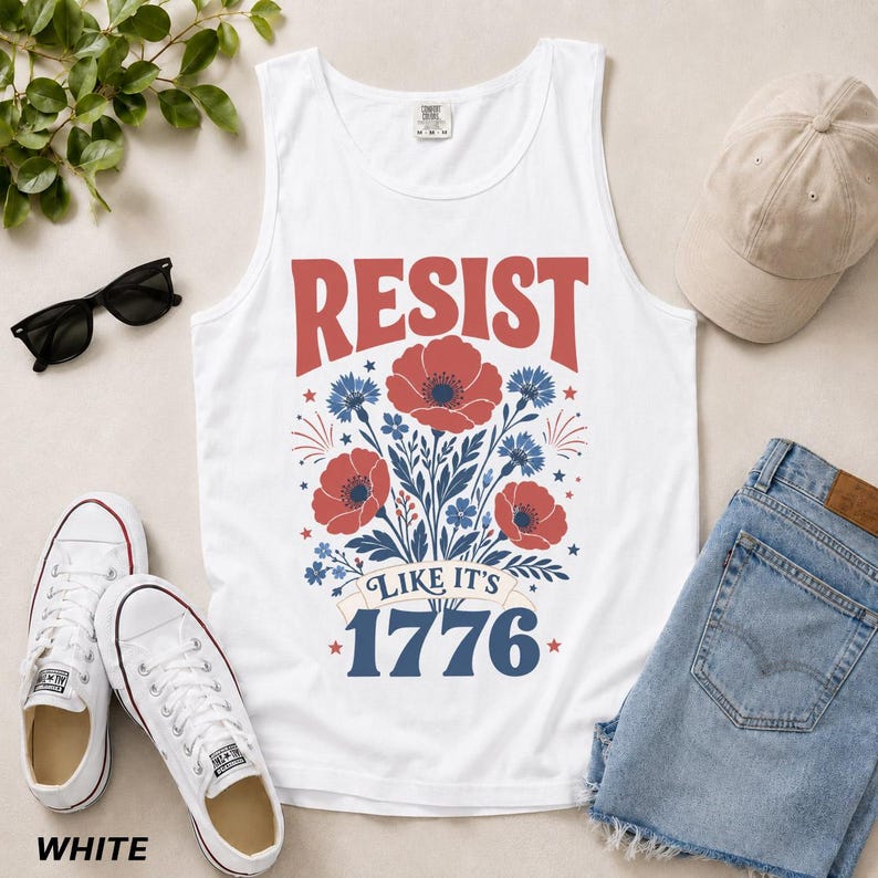 May include: A white tank top featuring a graphic print with the red text RESIST, blue text LIKE IT'S 1776, and a central illustration of red poppies and blue cornflowers. The design includes small star accents and decorative line work.