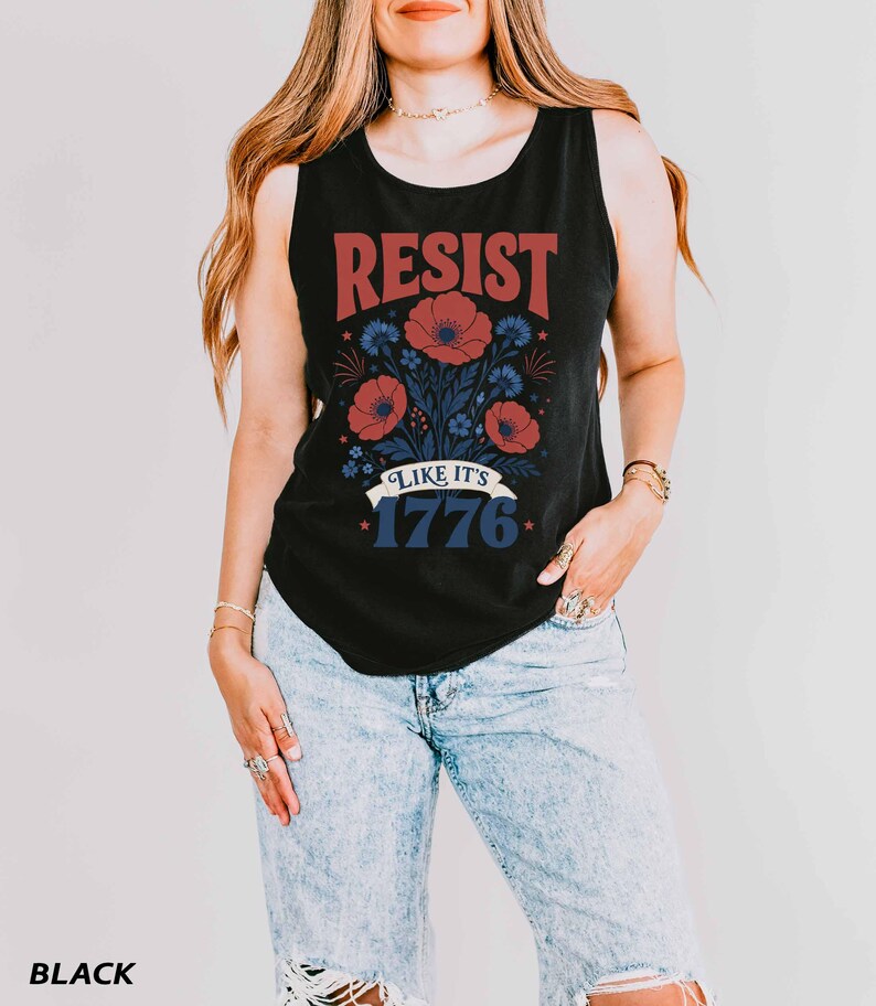 May include: A black sleeveless tank top featuring a graphic print with the red text RESIST above a floral illustration of red poppies and blue cornflowers. Below the flowers is a white banner with the blue text LIKE IT'S 1776 and small stars.