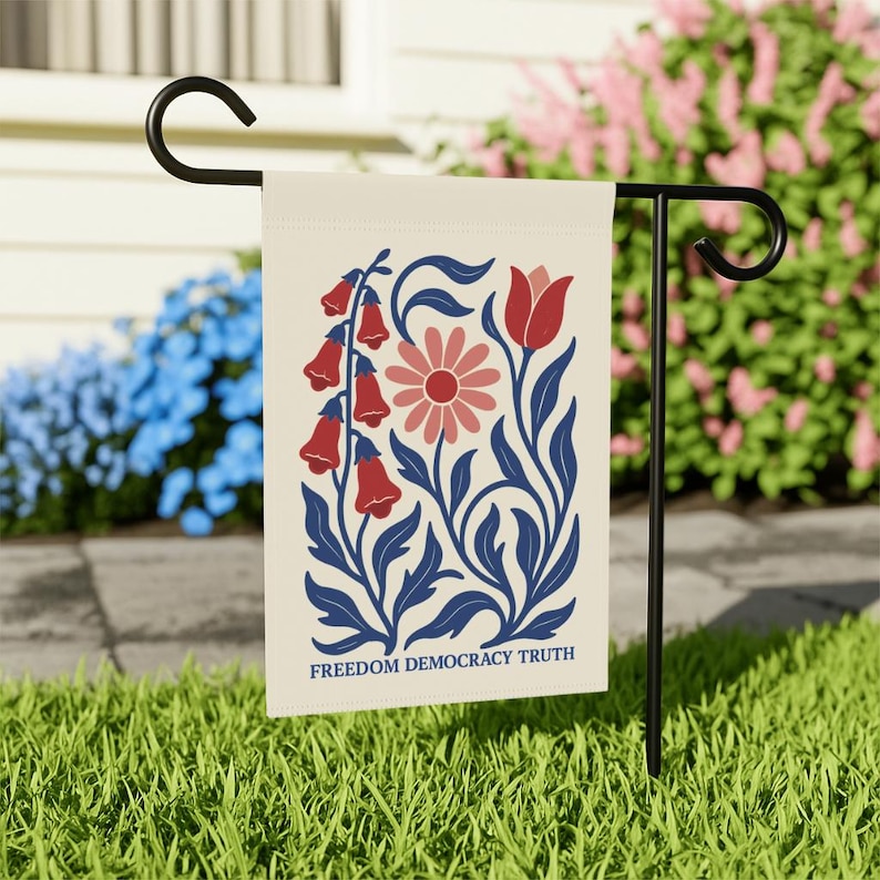 Peut inclure: Un drapeau de jardin rectangulaire suspendu &agrave; un support en m&eacute;tal noir, pr&eacute;sentant un fond cr&egrave;me avec une illustration florale en rouge, rose et bleu fonc&eacute;. Le motif inclut des fleurs en cloche, une marguerite et une tulipe, avec le texte FREEDOM DEMOCRACY TRUTH.