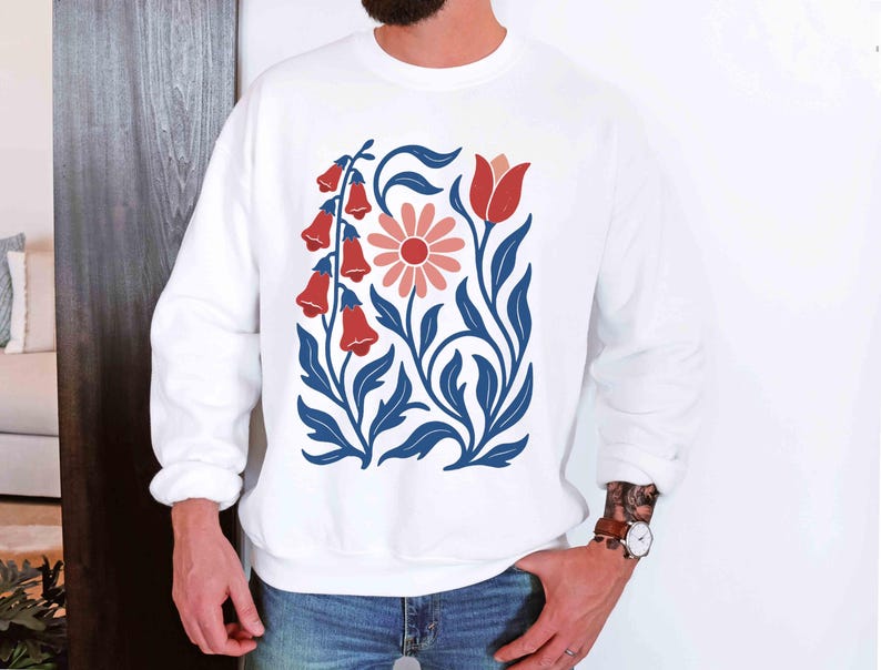 May include: White sweatshirt featuring a floral design with red bell-shaped flowers, a pink daisy, and blue leaves and stems. The design is centered on the front of the long-sleeved top. The sweatshirt is made of a soft material.