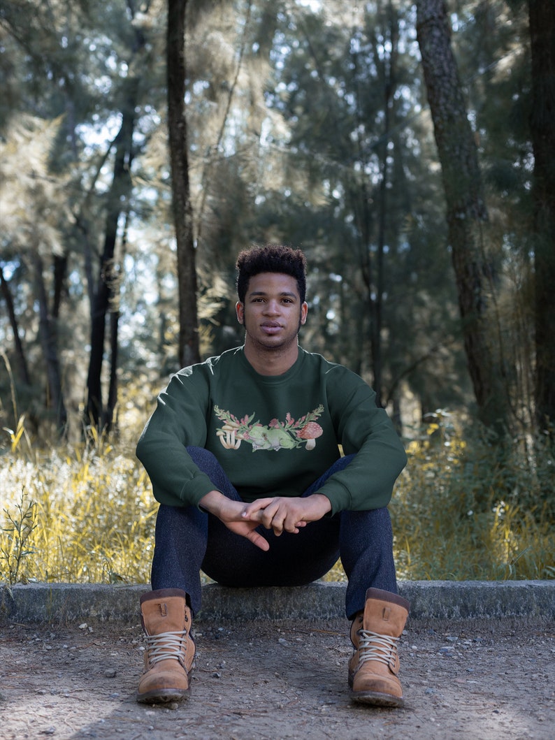 May include: A dark green sweatshirt with a mushroom and floral graphic print. The sweatshirt has a crew neck and long sleeves.
