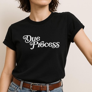 May include: Black t-shirt with white text that reads "Due Process" in a retro font.