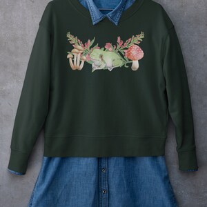 May include: A dark green sweatshirt with a watercolor design of a frog sitting on a branch with mushrooms and flowers.