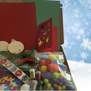 May include: A craft kit in an open cardboard box, containing red and green cardstock, wooden ornaments, stickers, glitter, pom-poms, and a handmade Christmas card with star and snowflake decorations. The background is a blue sky with snowflakes.