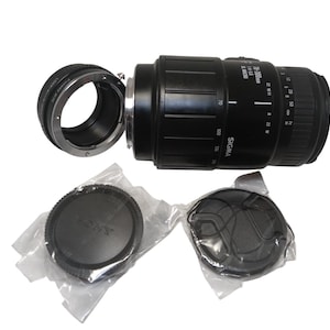 May include: A black Sigma 18-50mm f/3.5-5.6 DC lens with a lens adapter and two lens caps. The lens has measurement markings and the word "SIGMA" printed on it. The lens caps are black and one is labeled "SONY".
