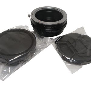 May include: A black and silver lens adapter with two black lens caps, all in clear plastic packaging. The adapter has the text "Fotasy M-R" and "LOCK" and "OPEN" labels. The caps are round and have a ridged edge.