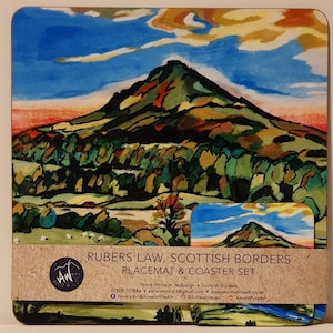 May include: A set of placemats and coasters featuring a colorful painting of Rubers Law, a mountain in the Scottish Borders. The artwork is in a stylized, almost abstract style, with a mix of green, brown, yellow, and blue hues. The text "Rubers Law, Scottish Borders Placemat & Coaster Set" is printed on a brown label at the bottom of the image.