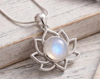 Puede incluir: Un collar de plata con un colgante en forma de flor de loto que presenta una piedra lunar redonda e iridiscente en el centro. El colgante está unido a una fina cadena de plata, mostrando un acabado de metal pulido y una gema suave.