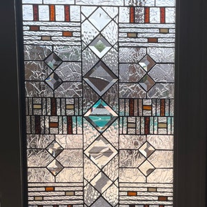 May include: A stained glass window with a geometric design featuring brown, orange, and white glass pieces. The window is divided into squares and diamonds.