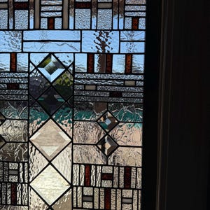 May include: A stained glass window with a geometric design featuring a variety of clear and brown glass pieces. The window is divided into squares and diamonds, creating a modern and abstract look.