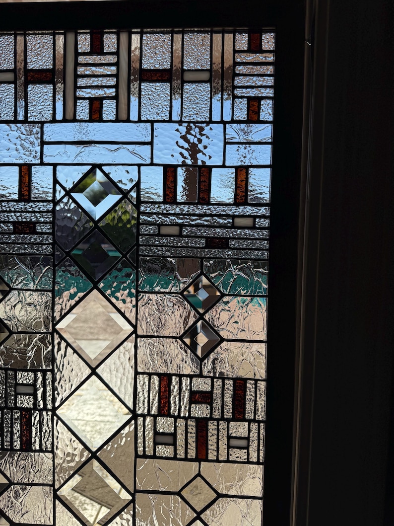May include: A stained glass window with a geometric design featuring a variety of clear and brown glass pieces. The window is divided into squares and diamonds, creating a modern and abstract look.