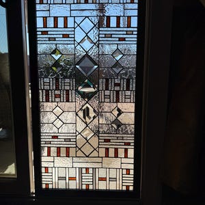 May include: A stained glass window with a geometric pattern in shades of brown, white, and clear glass. The window is framed in black.