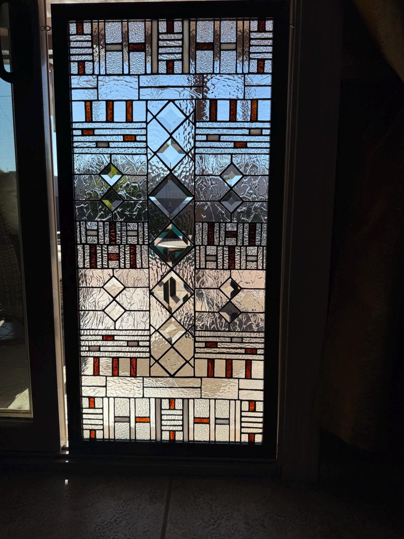 May include: A stained glass window with a geometric pattern in shades of brown, white, and clear glass. The window is framed in black.