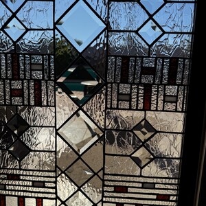 May include: A stained glass window with a geometric design featuring a mix of clear and textured glass. The window has a black frame and red accents.