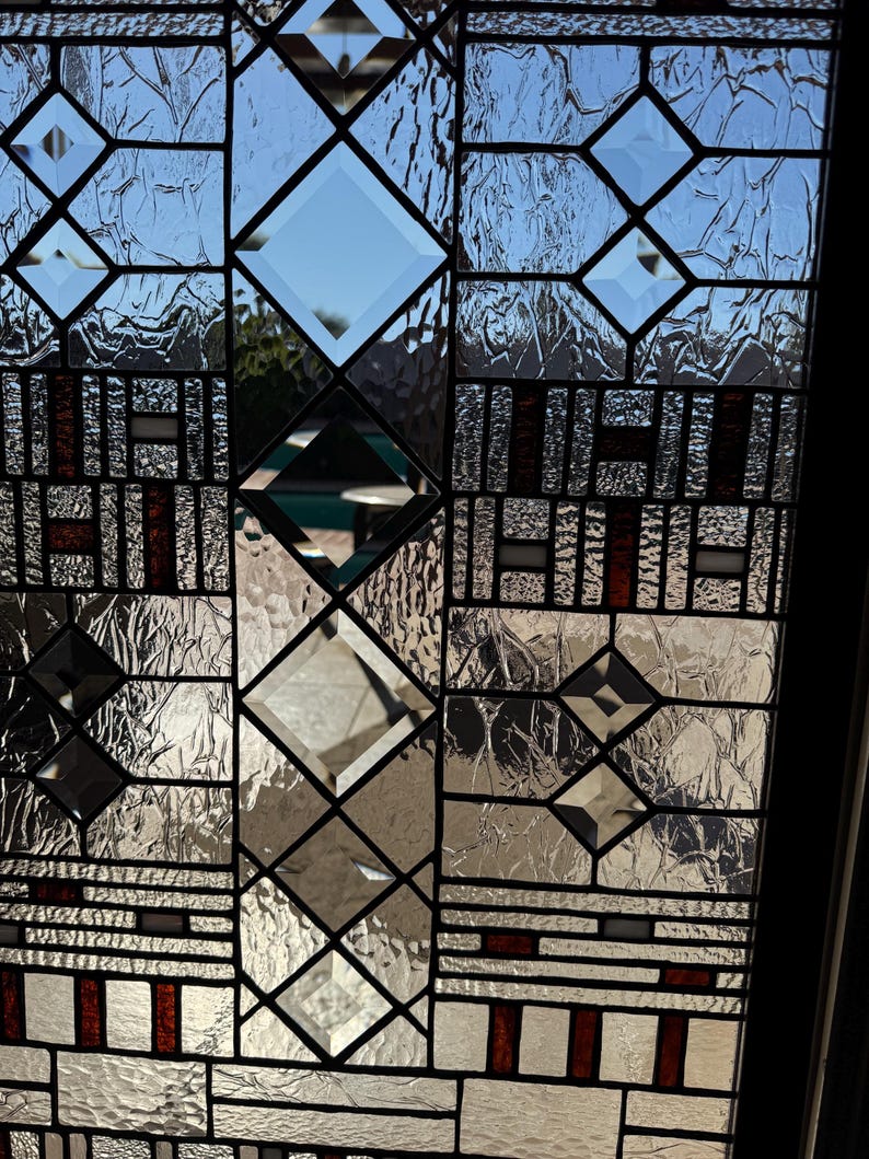 May include: A stained glass window with a geometric design featuring a mix of clear and textured glass. The window has a black frame and red accents.
