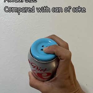 May include: A blue button-shaped lid on top of a silver can of Diet Coke. The text "Diet Coke" is visible on the can.