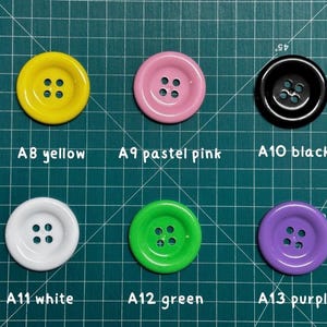 May include: Assortment of 6 round buttons in various colors, including yellow, pastel pink, black, white, green, and purple. Each button has four holes.