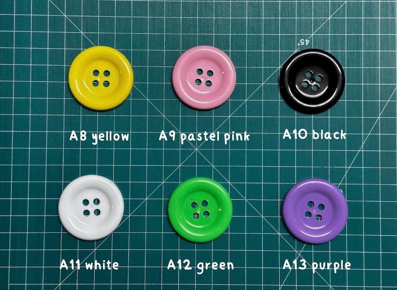 May include: Assortment of 6 round buttons in various colors, including yellow, pastel pink, black, white, green, and purple. Each button has four holes.