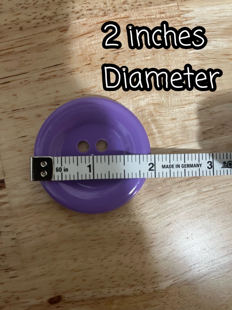 May include: A purple plastic button with two holes, measuring 2 inches in diameter. The button is on a wooden surface with a measuring tape.