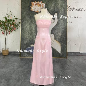 May include: A strapless, floor-length pink dress on a mannequin. The dress features a ruched bodice and embroidered floral details. The skirt is made of a sheer fabric. The words "Khimuki Style" are visible on the dress and in the background.