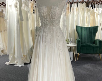 May include: A white tulle wedding dress with a beaded bodice and long sleeves. The dress is on a mannequin in a store setting. The text "Khimuki Style" is visible at the bottom of the image.