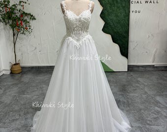 May include: A white tulle wedding dress with a lace bodice and a sweetheart neckline. The dress has a fitted bodice and a flowing skirt. The dress is on a mannequin in a studio setting.