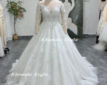 May include: A white wedding dress with long sleeves and a lace bodice. The dress has a full skirt and a train. The dress is on a mannequin in a store.