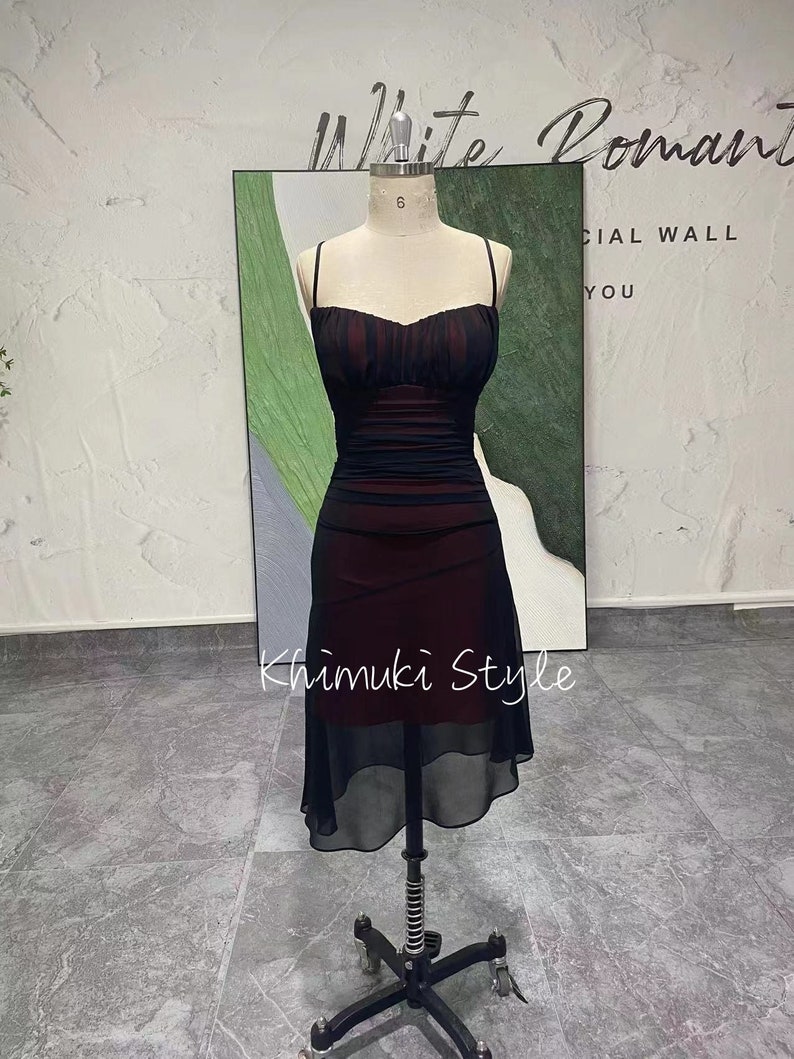 K&ouml;nnte beinhalten: Ein schwarzes und burgunderfarbenes Kleid mit einem figurbetonten Oberteil und einem flie&szlig;enden Chiffonrock. Das Kleid hat d&uuml;nne Tr&auml;ger und einen herzf&ouml;rmigen Ausschnitt.