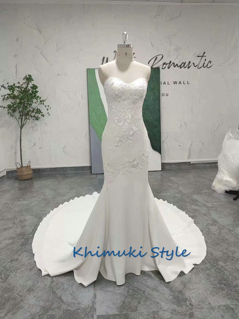 May include: A white strapless mermaid wedding dress with lace detailing and a flowing train. The dress is on a mannequin and the text "Romantic" and "Khimuki Style" is visible.