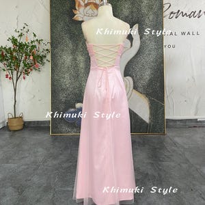 May include: A strapless, pale pink formal gown with a corset back and a flowing skirt. The dress is displayed on a mannequin. The text "Khimuki Style" is visible on the dress. The dress is floor-length and has a sheer overlay.