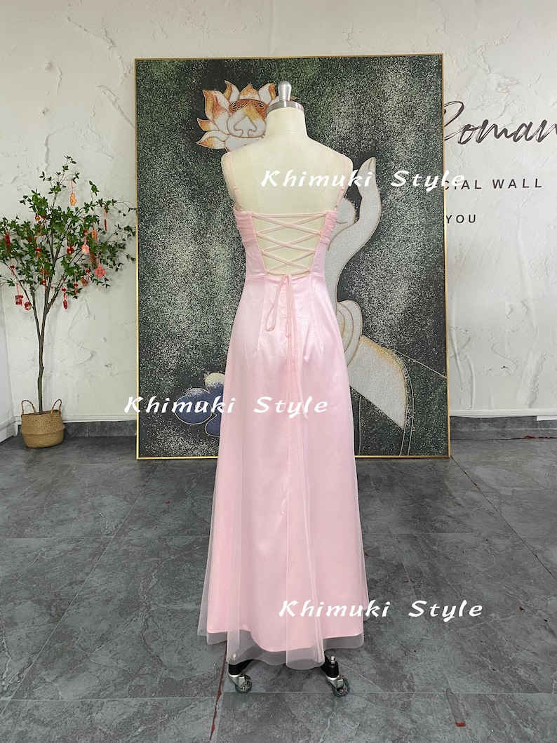 May include: A strapless, pale pink formal gown with a corset back and a flowing skirt. The dress is displayed on a mannequin. The text "Khimuki Style" is visible on the dress. The dress is floor-length and has a sheer overlay.