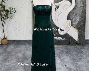 May include: A dark green, floor-length, sleeveless dress with black embroidery and a fitted bodice. The dress has a simple, elegant design and is perfect for a formal occasion.