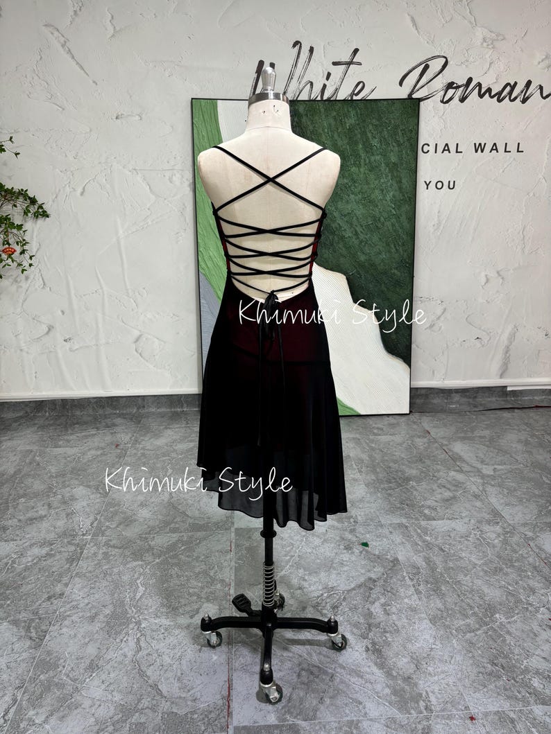 K&ouml;nnte beinhalten: Ein schwarzes und rotes Kleid mit Schn&uuml;rung am R&uuml;cken und einem Chiffonrock. Das Kleid befindet sich auf einer Puppe und der Hintergrund ist eine wei&szlig;e Wand.