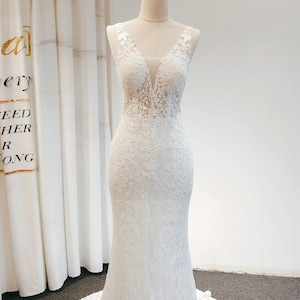 May include: A white lace wedding dress with a plunging neckline and a fitted bodice. The dress has a long train and is made of delicate lace.