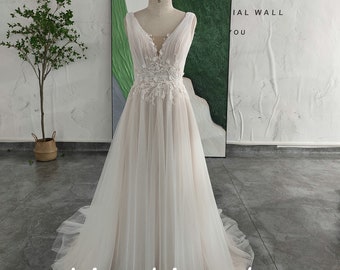 May include: A white tulle wedding dress with a V-neckline and lace detailing. The dress has a fitted bodice and a flowing skirt. The dress is displayed on a mannequin against a white wall. The text "White Romantic" and "Khimuki Style" is visible in the image.