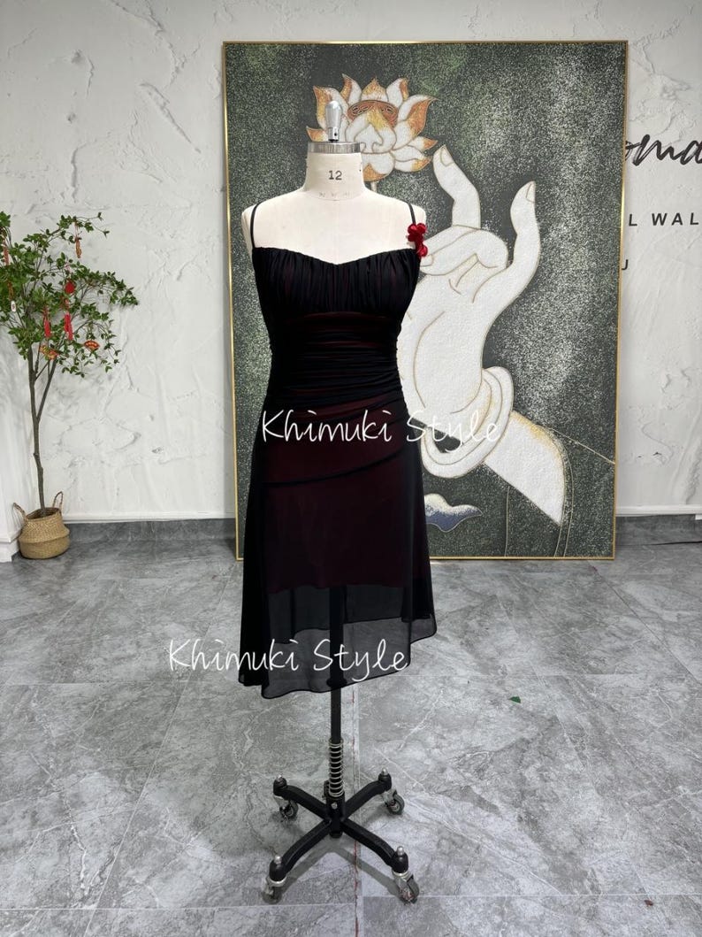 K&ouml;nnte beinhalten: Ein schwarzes und rotes &auml;rmelloses Kleid mit einem herzf&ouml;rmigen Ausschnitt und einem gerafften Rock. Das Kleid befindet sich auf einer Schaufensterpuppe und hat eine rote Blumenverzierung am Tr&auml;ger.