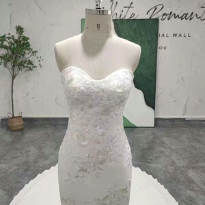 May include: A white strapless mermaid wedding dress with intricate lace detailing and a flowing train. The dress is displayed on a mannequin and the text "Khimuki Style" is visible at the bottom of the image.