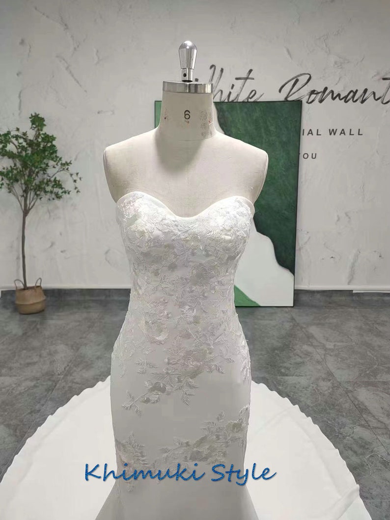 May include: A white strapless mermaid wedding dress with intricate lace detailing and a flowing train. The dress is displayed on a mannequin and the text "Khimuki Style" is visible at the bottom of the image.