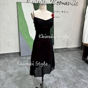 K&ouml;nnte beinhalten: Ein schwarzes Chiffonkleid mit gerafftem Oberteil und einem durchsichtigen &Uuml;berzug. Das Kleid hat eine rote Blumenverzierung am Oberteil und wird auf einer Schaufensterpuppe pr&auml;sentiert. Der Text "White Romantic" und "Khimuki Style" ist auf dem Bild zu sehen.