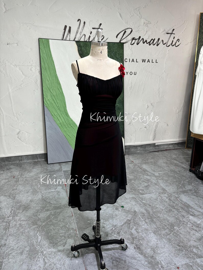 K&ouml;nnte beinhalten: Ein schwarzes Chiffonkleid mit gerafftem Oberteil und einem durchsichtigen &Uuml;berzug. Das Kleid hat eine rote Blumenverzierung am Oberteil und wird auf einer Schaufensterpuppe pr&auml;sentiert. Der Text "White Romantic" und "Khimuki Style" ist auf dem Bild zu sehen.
