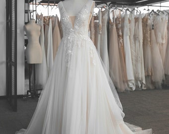 May include: A white tulle wedding dress with a V-neckline and a beaded bodice. The dress has a long train and is displayed on a mannequin in a bridal shop.