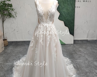 May include: A sleeveless ivory wedding dress with a plunging neckline and floral lace appliques. The dress features a flowing tulle skirt and a train. The text "Khimuki Style" is visible on the dress. The dress is displayed on a mannequin.