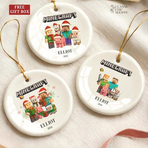 May include: White ceramic Minecraft Christmas ornaments with gold string hangers. Each ornament features a Minecraft character design, the word "Minecraft", the name "Elliot", and the year "2026". The top left corner has a "FREE GIFT BOX" label.