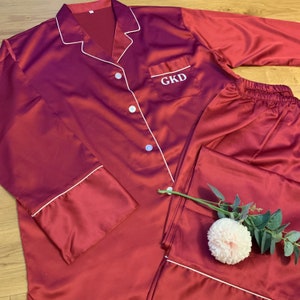 May include: Burgundy satin pajamas with white piping and a personalized pocket with the initials "GKD".